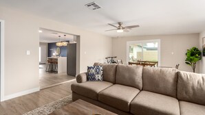 Ein geräumiges Wohnzimmer mit einem beigefarbenen Ecksofa, einem Holztisch und einem Deckenventilator.
