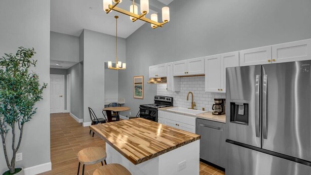 Una cocina moderna con armarios blancos, un refrigerador de acero inoxidable, una isla de madera y una lámpara colgante.