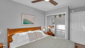 Un dormitorio con cama de madera, ventilador de techo, cuadro enmarcado, lámparas de noche y armario con espejo.