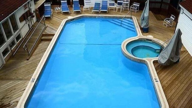 Ein rechteckiger Pool mit einer kleineren, runden Hottube, umgeben von einer Holzterrasse und Liegestühlen.
