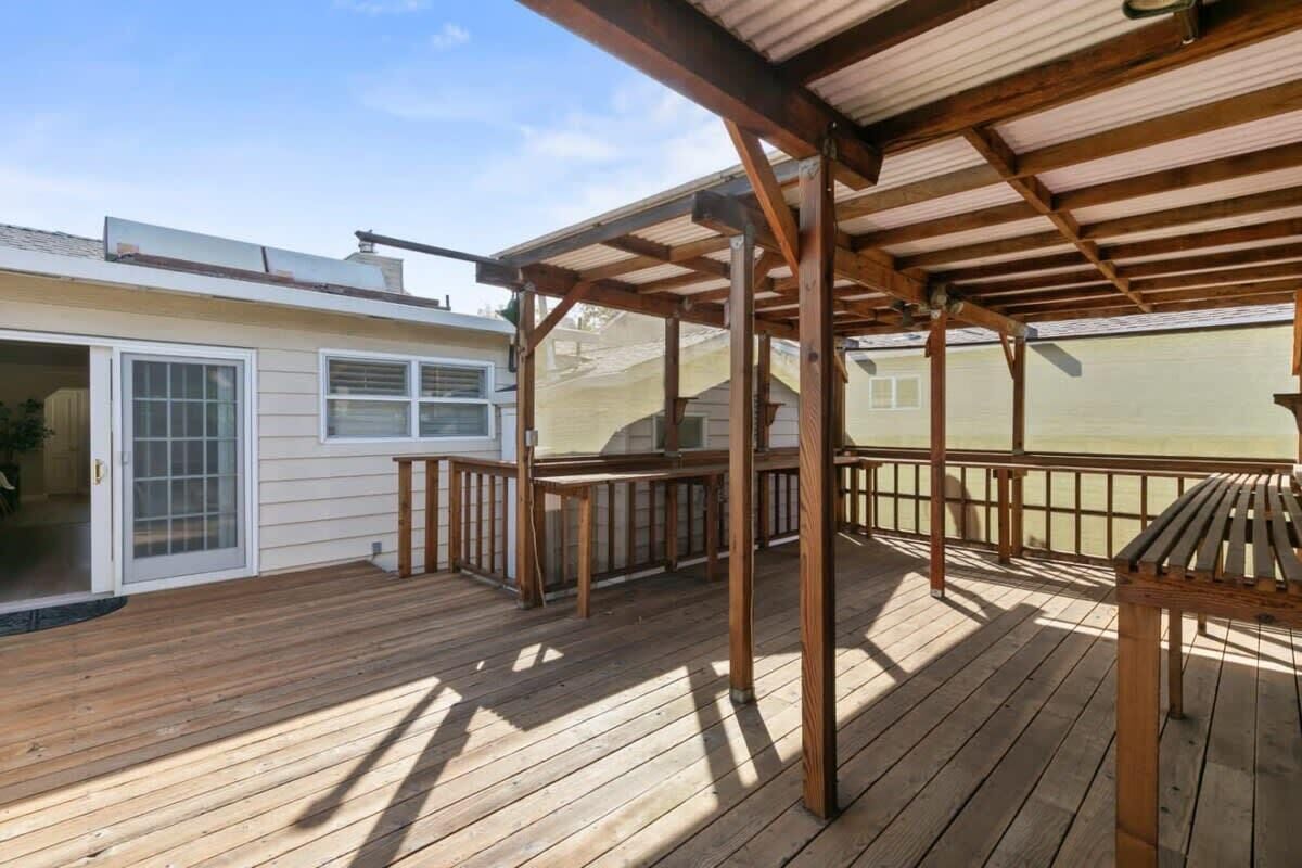 A wooden deck with a pergola, a sliding glass door, and a view of a neighboring house.