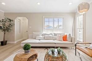 A modern living room with a white sofa, a glass coffee table, and a potted plant. - Marbella Lane - Modern Refreshing Home (San Mateo)