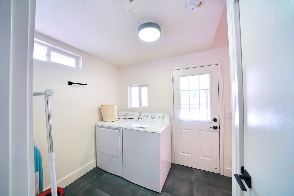 A laundry room with two white washers and dryers, a mop, and a door with a window.
