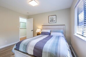 A bedroom with a bed, a nightstand, a lamp, a framed picture on the wall, and a window with blinds. - Marbella Lane -siliconvalley 3BR Gem in SJ (San Jose)