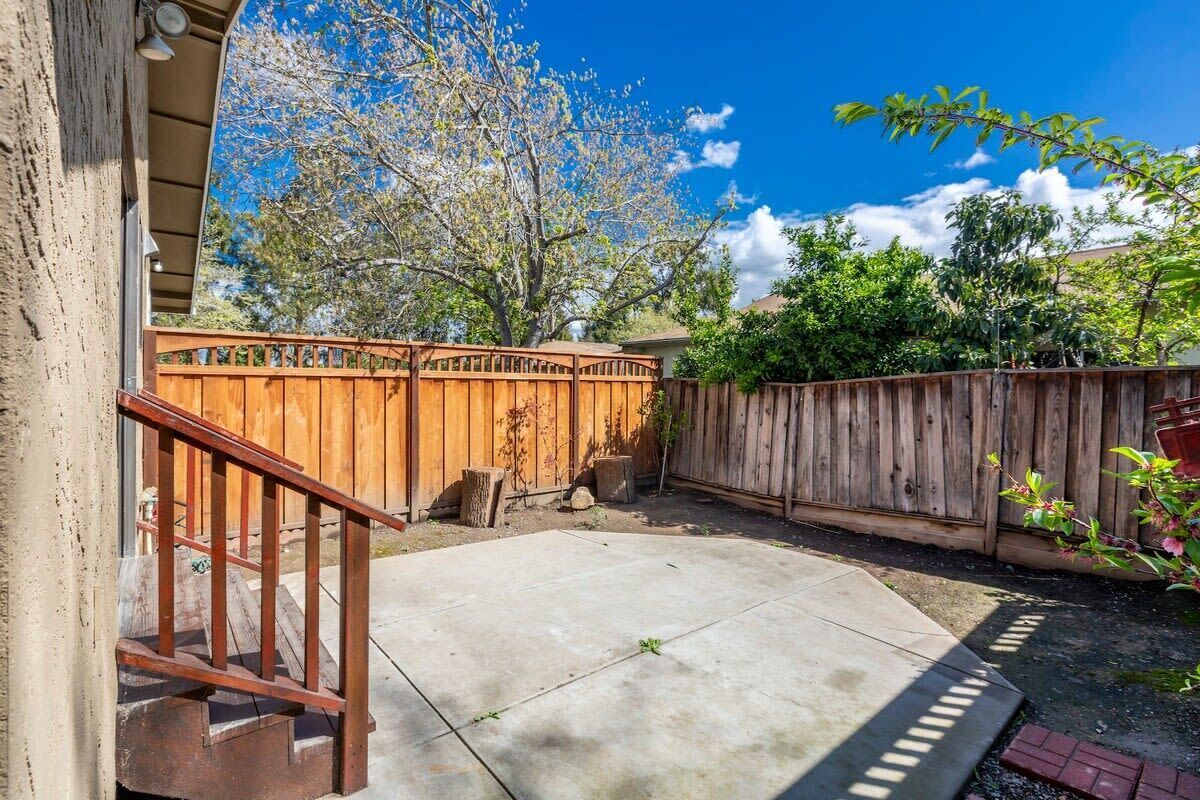 A backyard with a wooden fence, a concrete patio, and a staircase leading to a house.