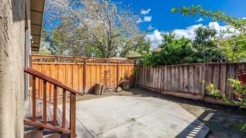 A backyard with a wooden fence, a concrete patio, and a staircase leading to a house.