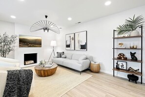 Un salon moderne avec un canapé blanc, une table basse ronde en bois et une statuette de chat noir posée sur une étagère.