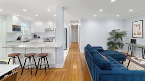 Una cocina moderna con armarios blancos, encimera de mármol y una isla central con taburetes.