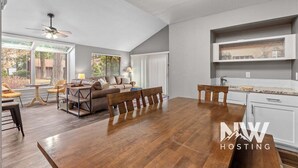 A spacious living area with a dining table, sofa, and chairs, a kitchen with a built-in shelf, and a ceiling fan. - Twin Lakes Village Home Golf Retreat Community Pool Corner Lot and Single Level Living (Rathdrum)