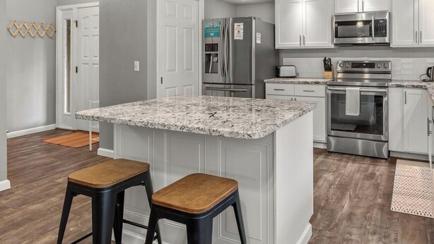 A modern kitchen with white cabinets, stainless steel appliances, and a granite island with stools. - Twin Lakes Village Home Golf Retreat Community Pool Corner Lot and Single Level Living (Rathdrum)