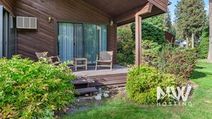 A wooden cabin with a covered porch, two wicker chairs, and a small table. - Twin Lakes Village Home Golf Retreat Community Pool Corner Lot and Single Level Living (Rathdrum)
