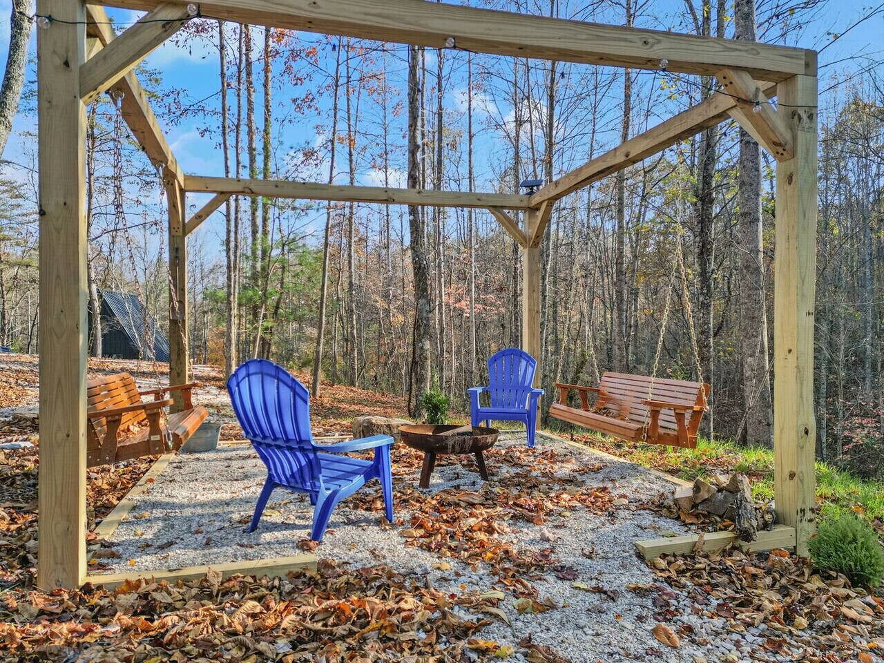 A wooden gazebo with two blue Adirondack chairs and a wooden bench.