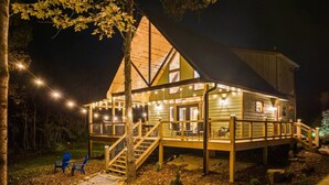A wooden cabin with a deck, outdoor seating, and string lights. - Wifi, Hot Tub & Pets - Eaglerock Retreat in Rrg! (Rogers)