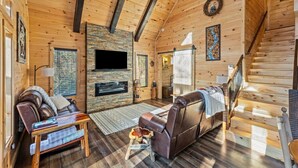 A cozy log cabin interior with a fireplace, leather sofa, and a staircase. - Wifi, Hot Tub & Pets - Eaglerock Retreat in Rrg! (Rogers)