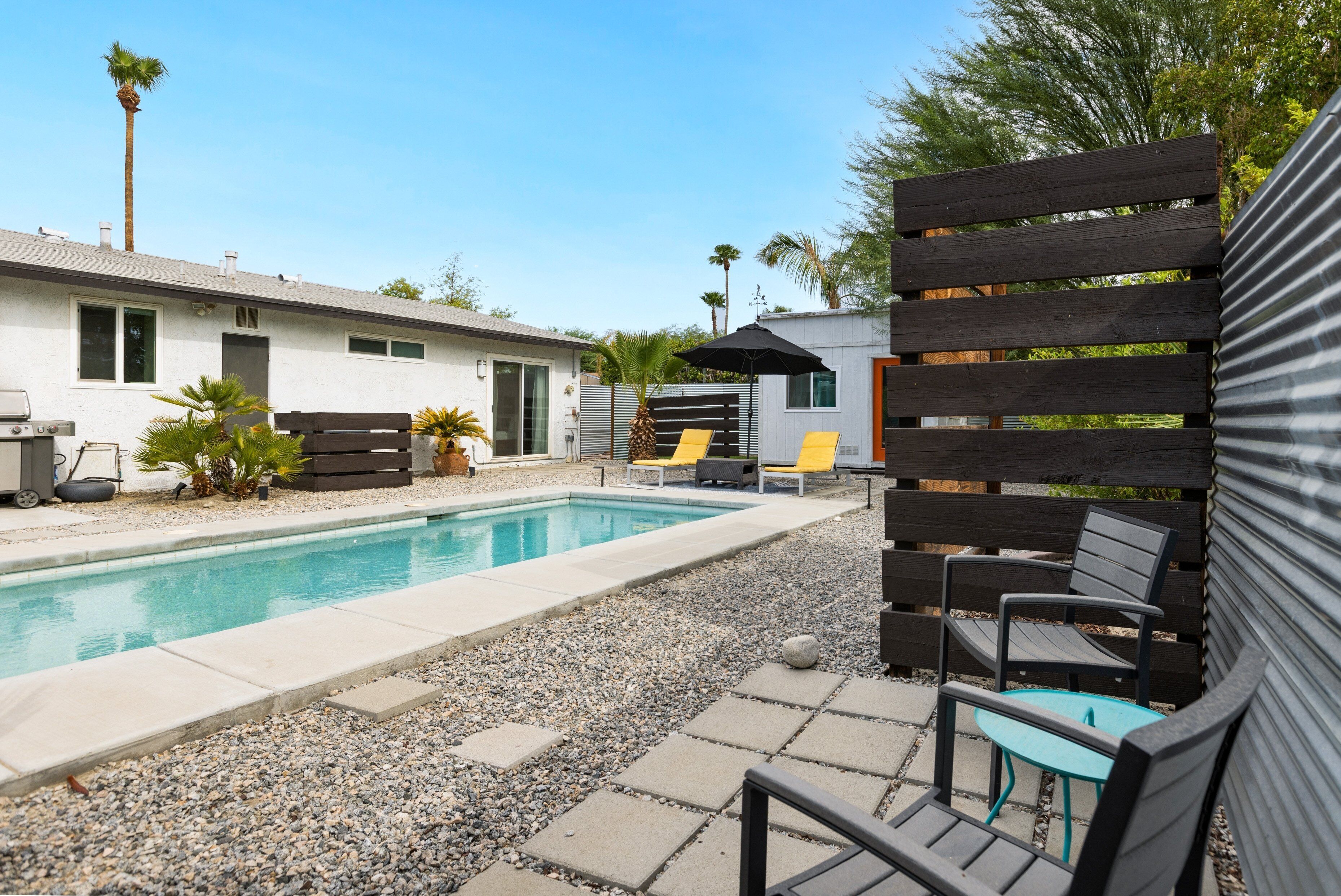 Un área de piscina con una piscina rectangular, sillones de descanso y una estructura de pérgola.