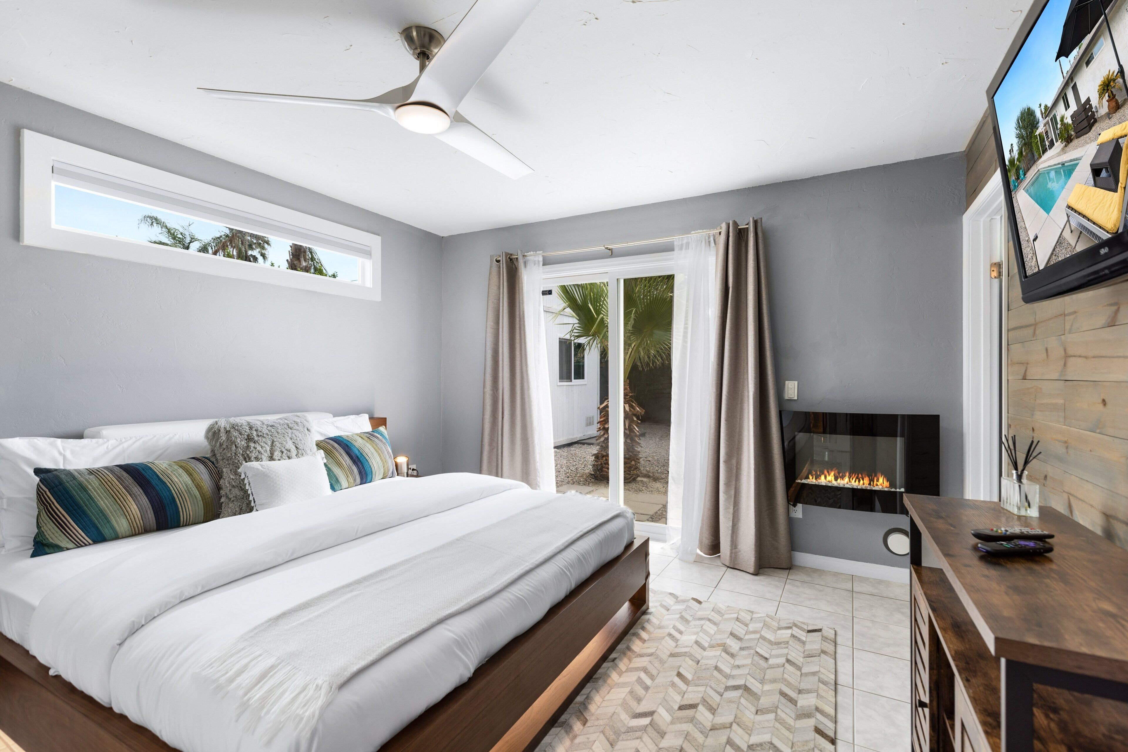 Un dormitorio con cama, ventilador de techo, chimenea y televisor montado en la pared.