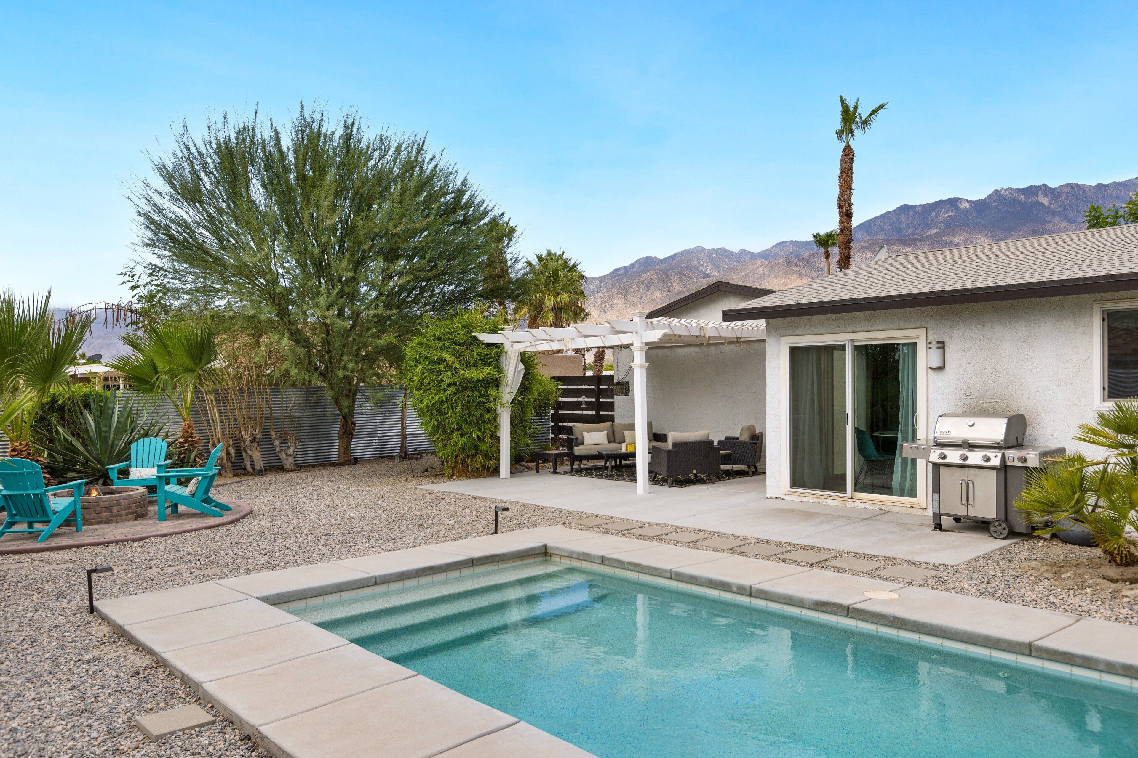 A backyard with a swimming pool, outdoor furniture, and a barbecue grill.