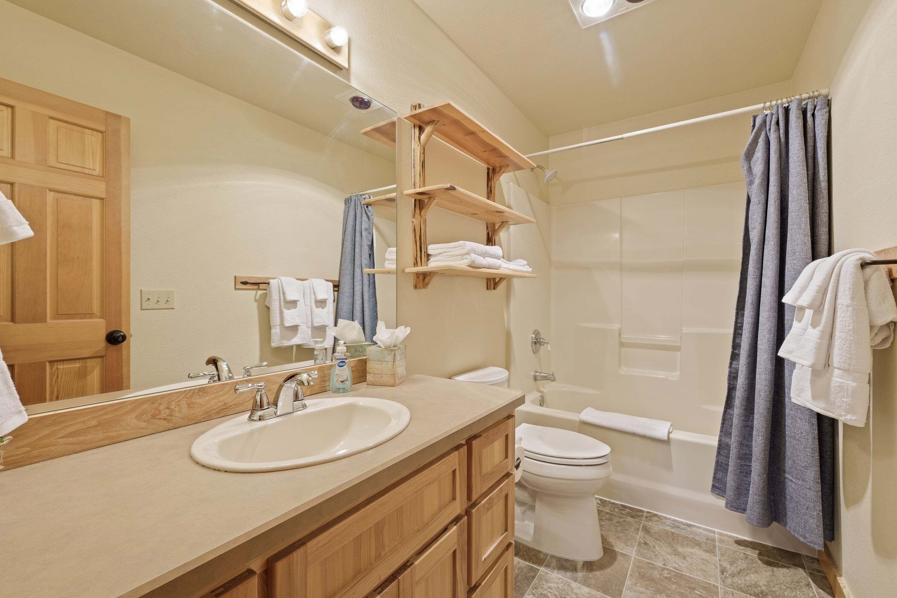 A bathroom with a wooden vanity, a sink, a toilet, a shower with a curtain, and a mirror.
