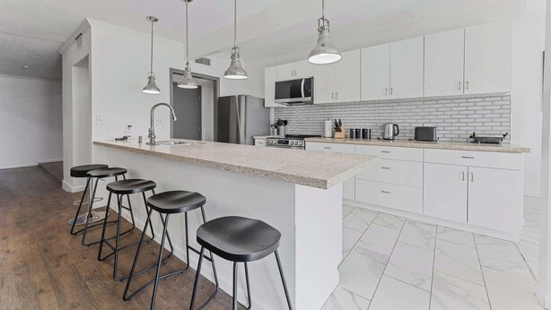 A modern kitchen with white cabinets, a granite countertop, stainless steel appliances, and black bar stools.