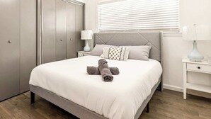 A neatly made bed with a grey headboard, a bedside table with a lamp, and a wardrobe with a mirror.