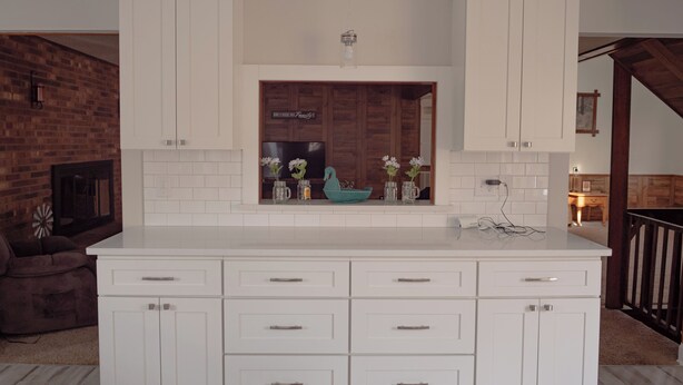 Een keuken met witte kasten, een centraal eiland met lades en een bakstenen muur op de achtergrond.