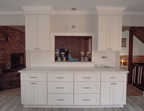 A kitchen with white cabinetry, a central island with drawers, and a brick wall in the background. - Rustic, wooded getaway nestled in the outskirts of Forsyth County (Rural Hall)