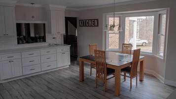 Une cuisine moderne avec des meubles blancs, une table à manger avec des chaises et une grande fenêtre donnant sur l’extérieur.