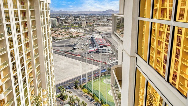 A high-rise building with multiple floors, large windows, and a view of a cityscape including roads, a sports field, and distant mountains. - Spacious MGM Studio Topgolf Pool Views 07718 (Las Vegas)