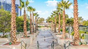 A pathway lined with palm trees and planters, leading to a building with a glass facade. - Spacious MGM Studio Topgolf Pool Views 07718 (Las Vegas)