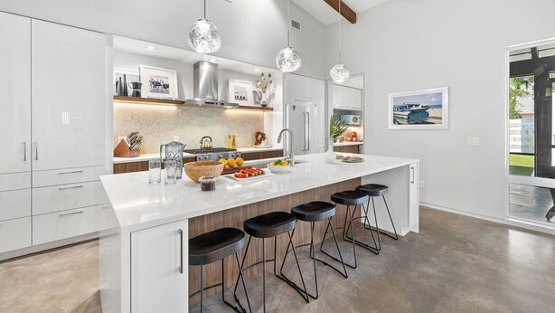 Een moderne keuken met witte kasten, een groot eiland met barkrukken, hanglampen en uitzicht op het omliggende landschap.