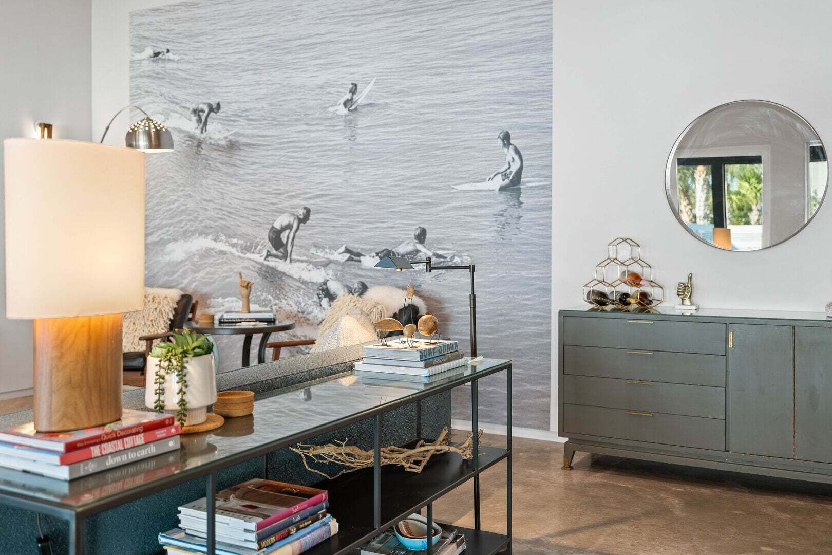 Een moderne woonkamer met een groot abstract schilderij, een glazen salontafel, een lamp en een grijze kast.