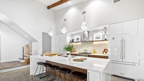 Een moderne keuken met een centraal eiland, barkrukken, roestvrijstalen apparatuur en hanglampen.