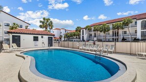 A swimming pool with lounge chairs, a fenced area, and multi-story buildings with red-tiled roofs. - Sea Palms (Santa Rosa Beach)