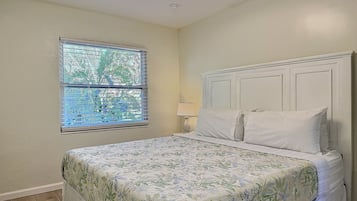 A bedroom with a bed, a window with blinds, a nightstand, and a lamp.