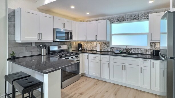 A modern kitchen with white cabinets, a black countertop, stainless steel appliances, and a wooden floor. - Siesta Heron 3 (Siesta Key)
