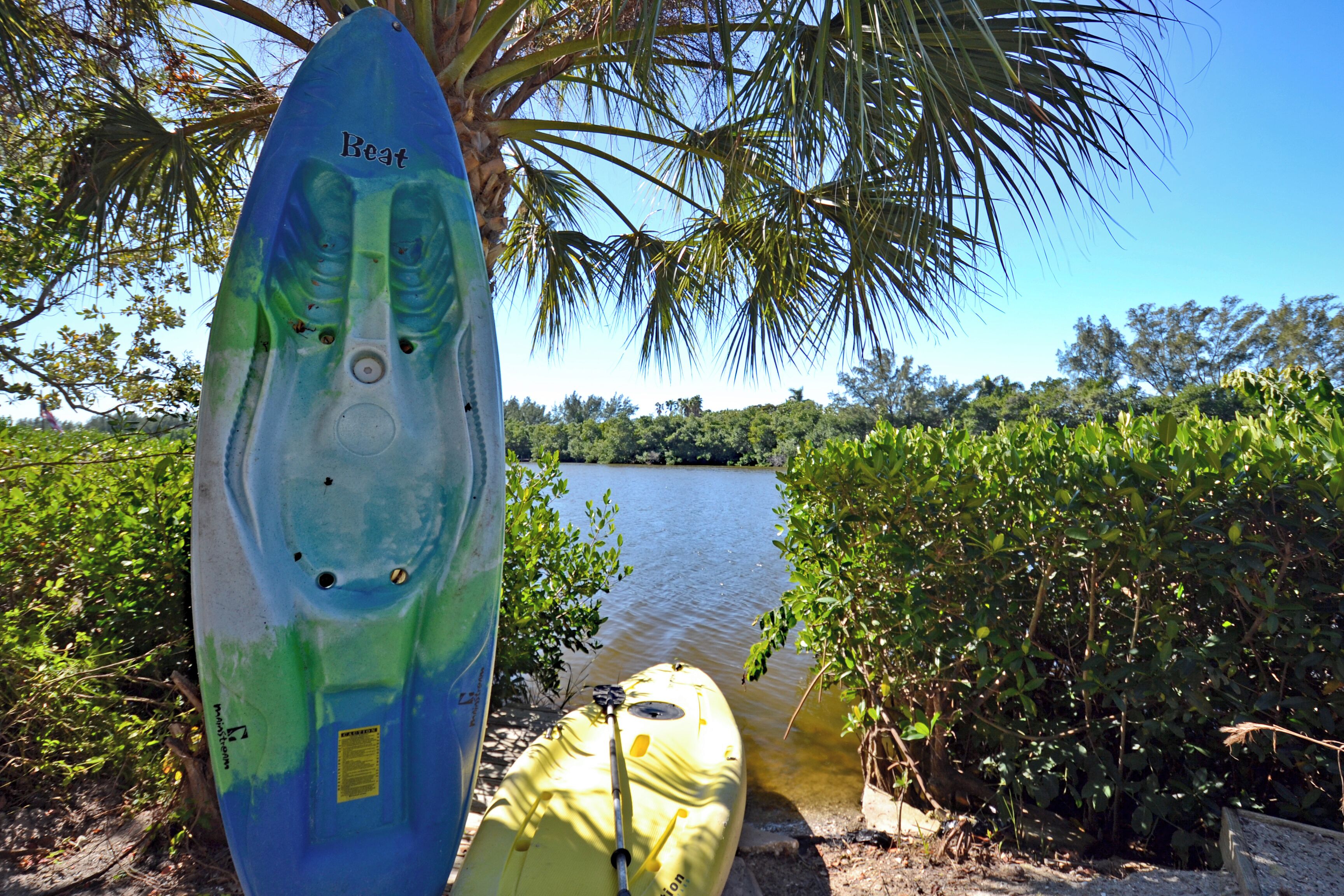 A kayak with a blue and green design, a yellow kayak, and a body of water surrounded by greenery.