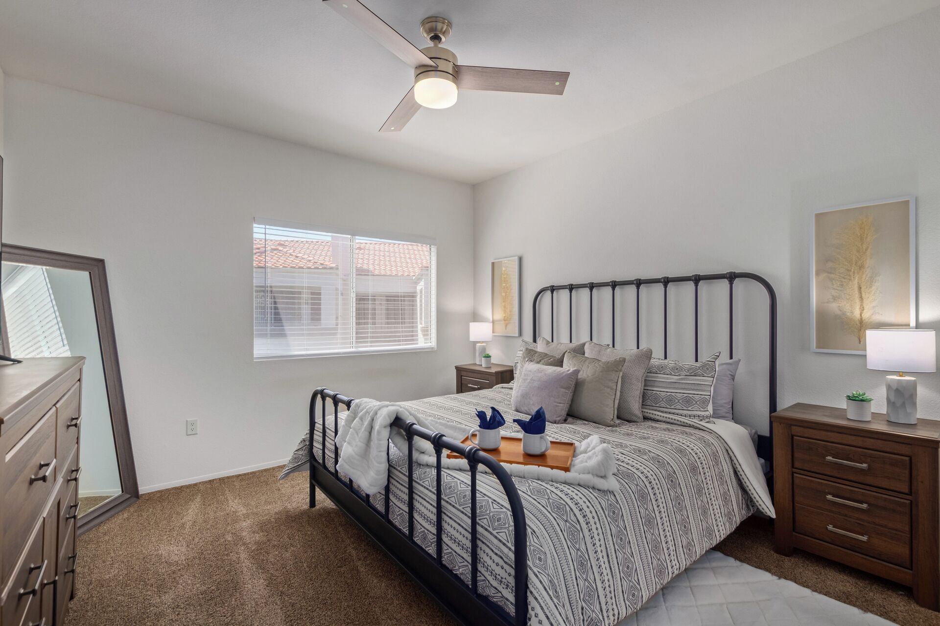 Un dormitorio con cama, mesitas de noche, cómoda, ventilador de techo y ventana con persianas.