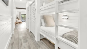 Ein modernes, weißes Schlafzimmer mit Etagenbetten, Holzboden und Blick ins Freie.