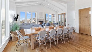 A spacious dining area with a long wooden table, wicker chairs, and a view of the ocean through large windows. - Salt & Light (Santa Rosa Beach)