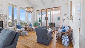 A spacious living area with large windows, wicker furniture, and a view of the ocean. - Salt & Light (Santa Rosa Beach)
