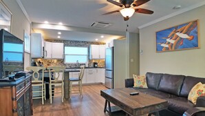 A modern kitchen with white cabinets, a central island, and a dining area with wooden chairs. - Siesta Heron 2 (Siesta Key)