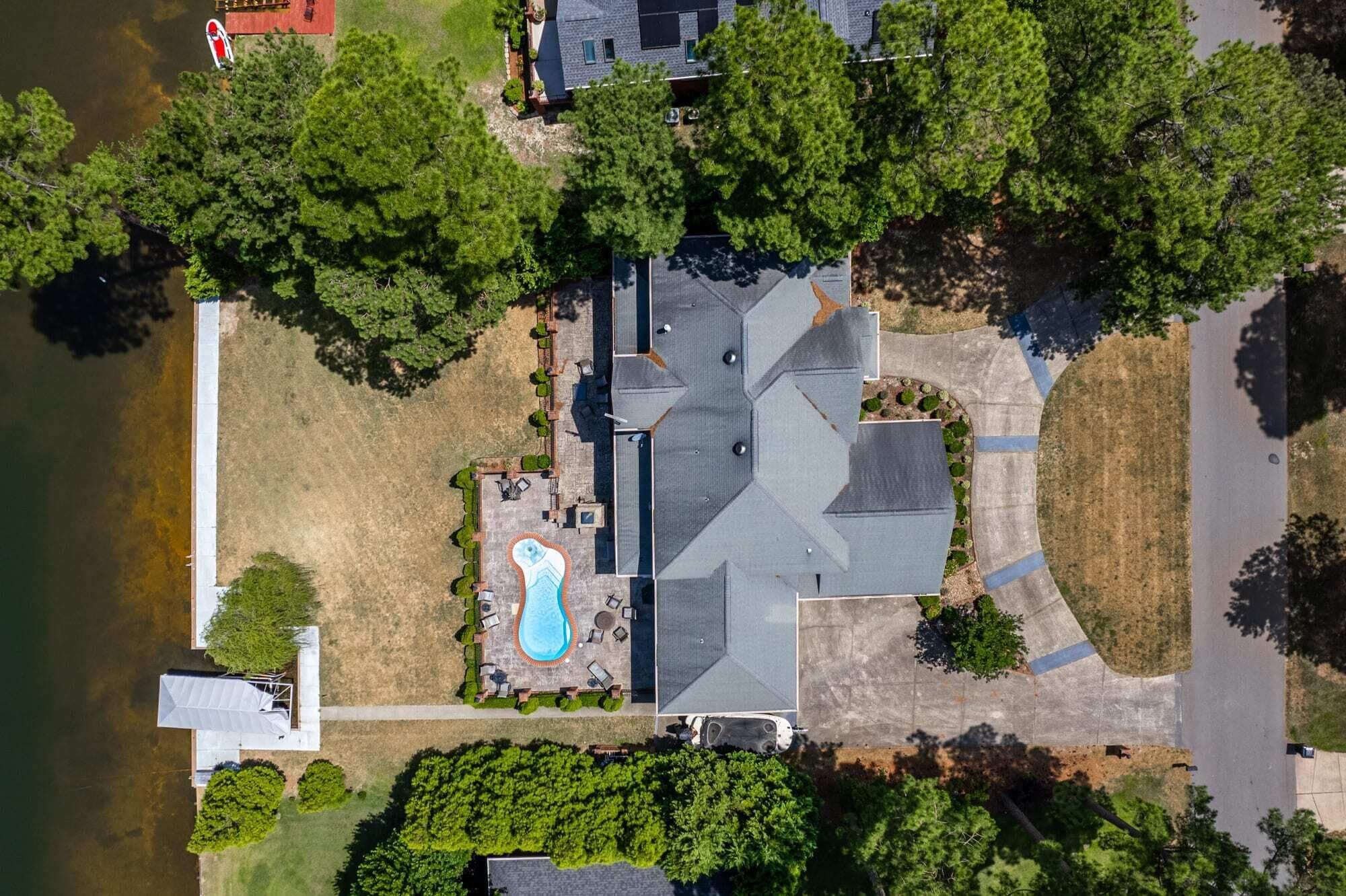 An aerial view of a house with a swimming pool, surrounded by trees and a body of water.