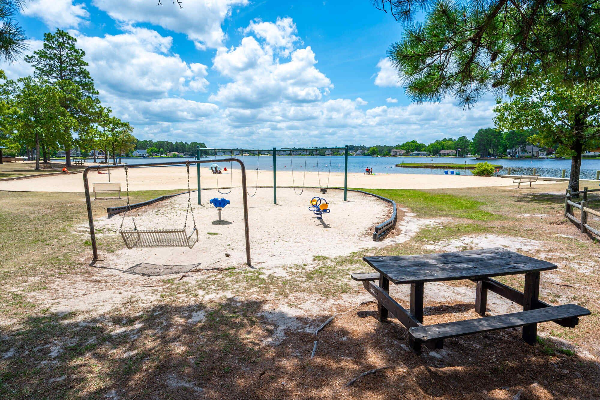 Un parque con zona arenosa, columpios, un banco y una mesa de picnic.