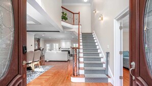 Un intérieur spacieux avec un plancher en bois, un escalier recouvert d’une moquette à motifs et un coin cuisine visible au fond.