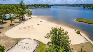 Une plage au bord d’un lac, avec un filet de volley-ball, des tables de pique-nique et une aire de jeux pour enfants.