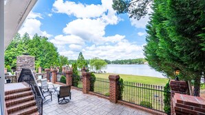 Une terrasse avec mobilier d’extérieur, une cheminée en pierre et une vue sur un lac.