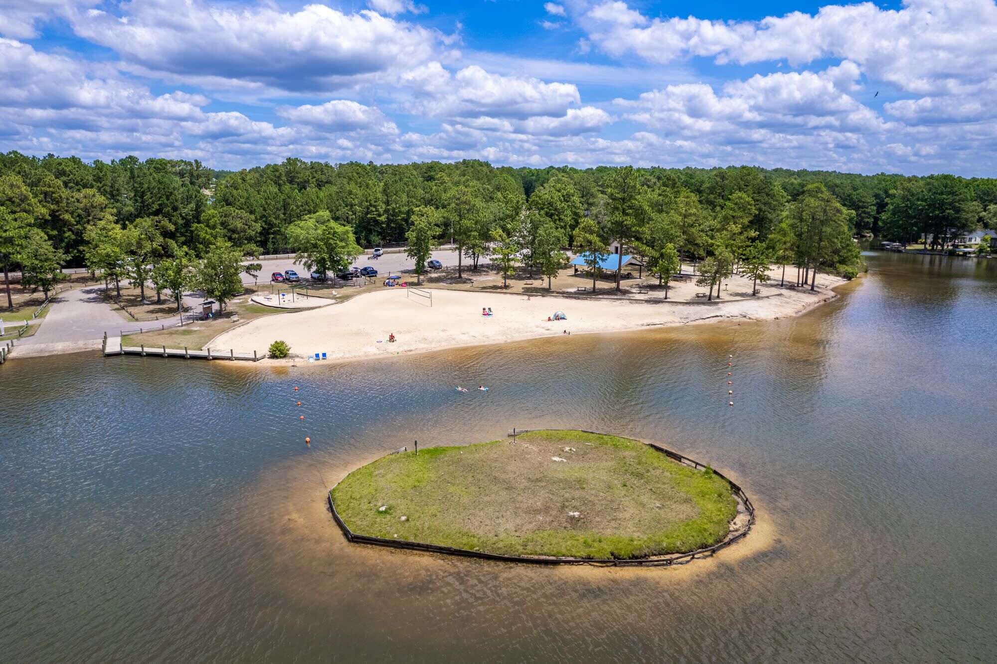 A lakeside park with a sandy beach, picnic areas, and a small island.