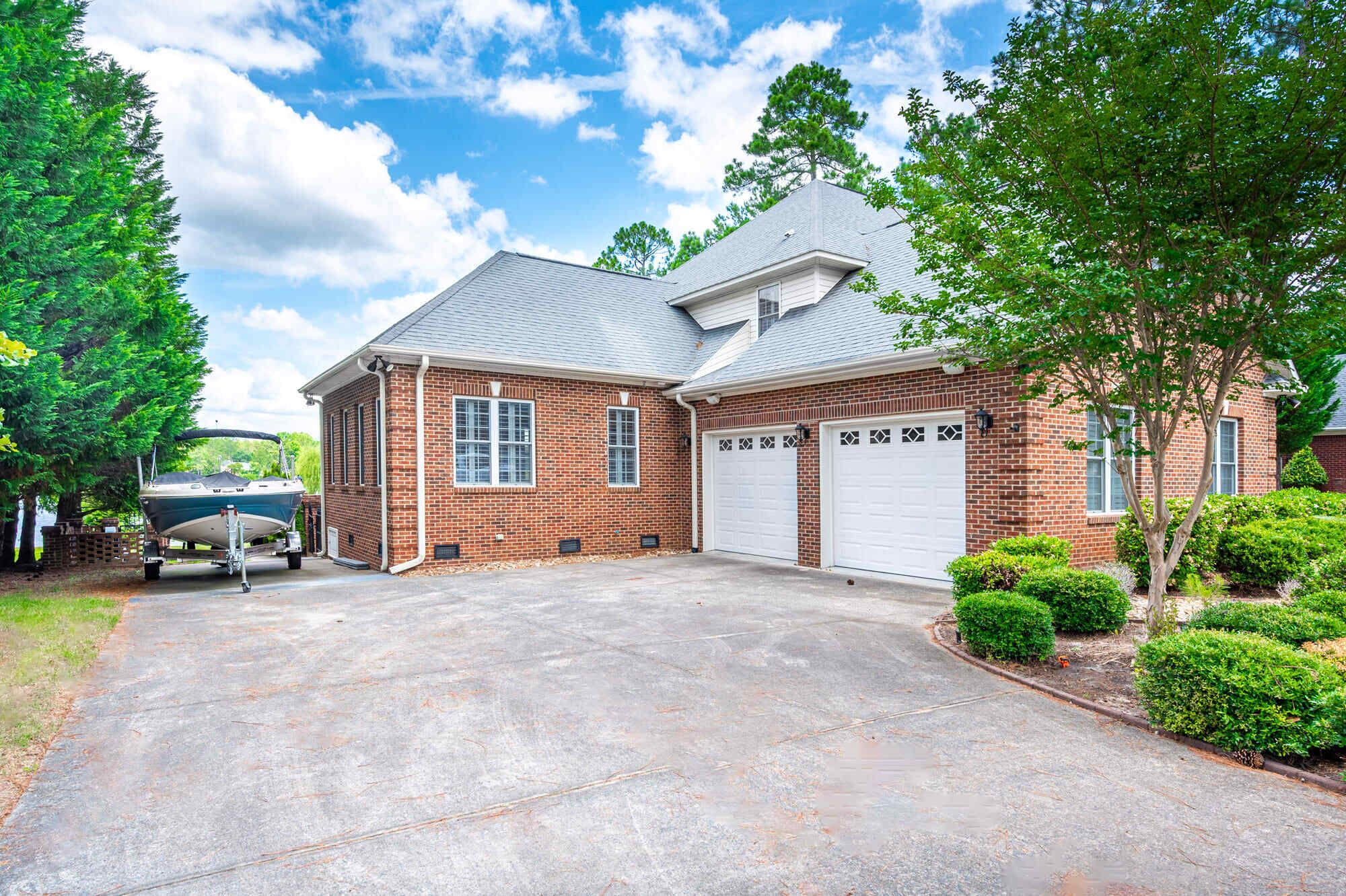 A two-story brick house with a garage, a boat in the driveway, and well-maintained landscaping.