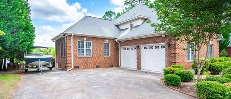 A two-story brick house with a garage, a boat in the driveway, and well-maintained landscaping.