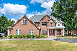 A two-story brick house with a front porch, a garage, and a well-maintained lawn. - Private Pool! Wateredge Lake House (Sanford)